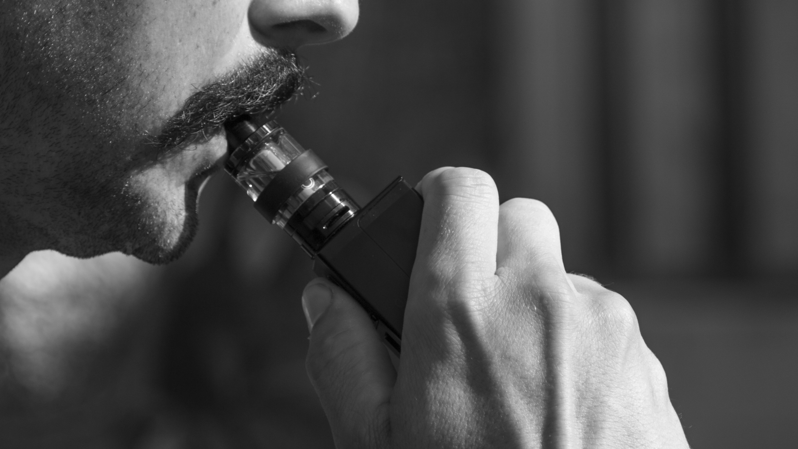 Black and white close-up photo of a man exhaling vapor from an electronic cigarette.