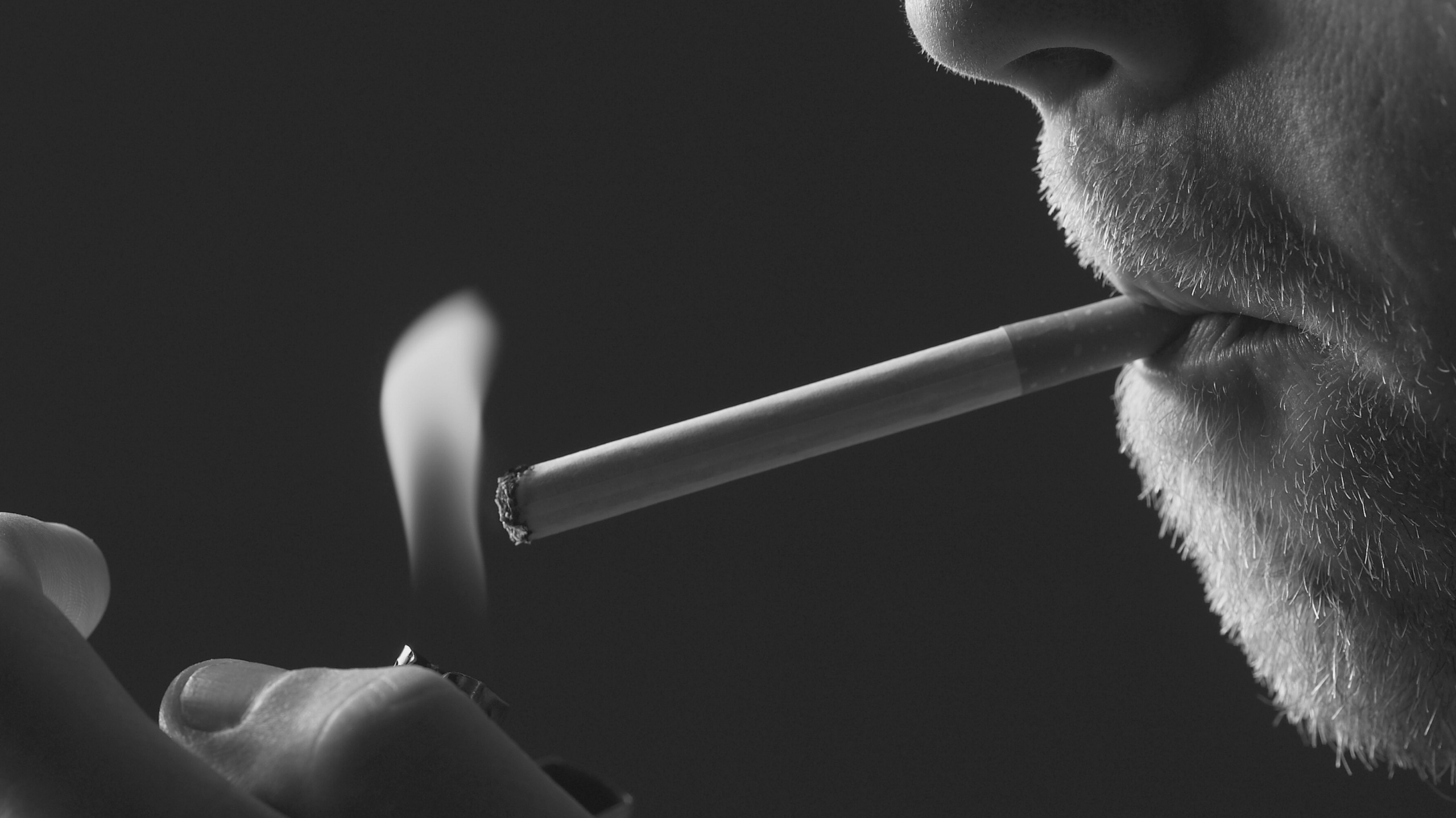 Black and white closeup photograph of a hand holding a cigarette with rising smoke.